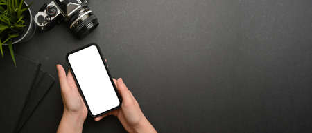 Overhead shot of female hands using smartphone include clipping path on dark workspace with camera