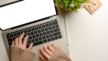 Top view of female hands typing on laptop keyboard on white table decorated with plant pot, clipping pathの写真素材