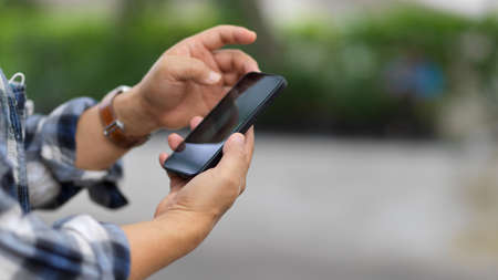 Side view of male hands texting message on smartphone while outdoor standingの写真素材