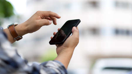 Side view of male hands texting message on smartphone while outdoor standingの写真素材