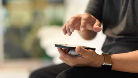 Close up view of a man using smartphone while sitting in blurred backgroundの写真素材