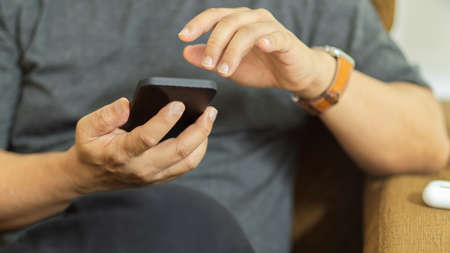 Cropped shot of male using smartphone while relaxed sitting on sofa in living roomの写真素材