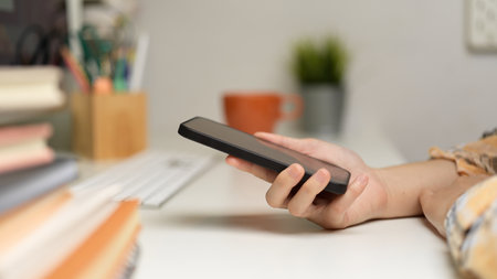 Side view of female freelancer hand holding smartphone on computer desk in home office roomの写真素材