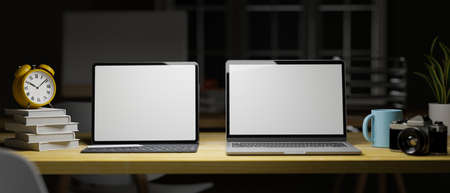 3D rendering, two laptops with mock-up screen on wooden table with stack of books, supplies and clock in home office at night, 3D illustrationの写真素材