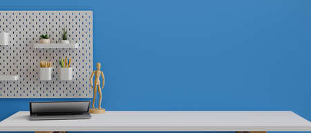 Stylish working desk with laptop, wooden figure, copy space and stationery on the shelf on blue wall, 3D rendering, 3D illustrationの写真素材