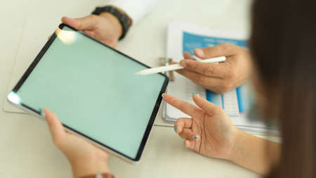 Side view of two people hands using digital tablet on white table with paperworkの写真素材