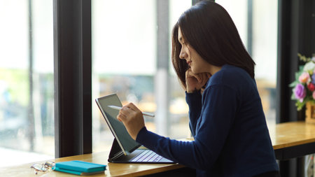 Side view of female teenager using digital tablet with stylus and keyboard in coffee shopの写真素材