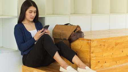 Female teenager with school bag using smartphone while relaxed sitting in universityの写真素材