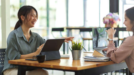 Side view of two female workers smiling and talking to each other while meeting on their projectの写真素材