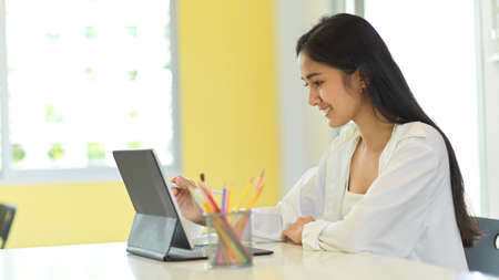Side view of female student using digital tablet while studying in classroomの写真素材