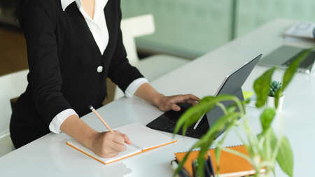 Cropped shot of businesswoman hands working with digital tablet and writing on notebook at workplaceの写真素材