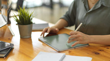Close up view of female hands using digital tablet on wooden workspace with office suppliesの写真素材