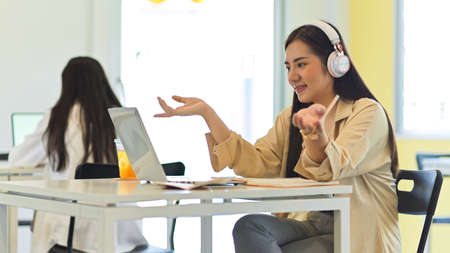 Portrait of female student speaking while online studying on laptop in co-working spaceの写真素材