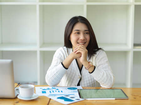 Portrait of female worker smiling and looking outside while sitting in workplaceの写真素材