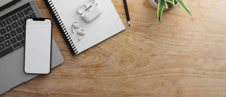 Smartphone with mock-up screen on laptop keyboard on wooden table with notebook and earphones, 3D...