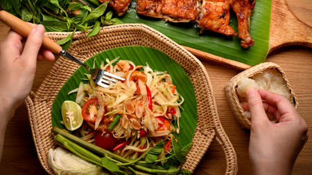 Female hands with fork and sticky rice eating papaya salad (Somtum) and Thai style grilled chicken, top viewの写真素材