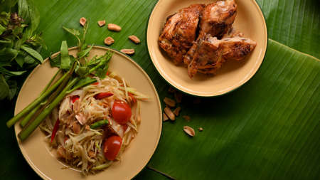 Thai food, papaya salad (Somtum) serving with Thai style grilled chicken on banana leaves backgroundの写真素材