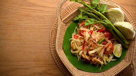 Somtum or papaya salad with vegetables on wicker plate on wooden table, Thai foodの写真素材