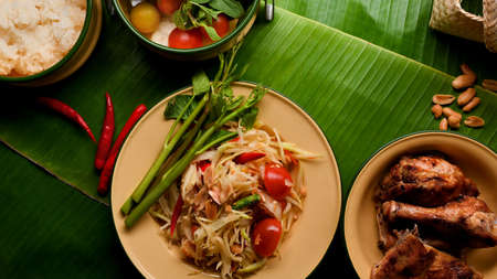 Thai food, papaya salad (Somtum) serving with Thai style grilled chicken and sticky rice on banana leaves backgroundの写真素材