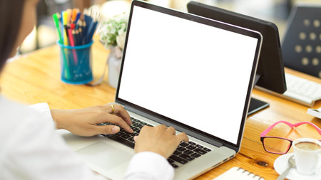 Over shoulder close up view of female hands typing on laptop with mock-up screen on office desk with stationeryの写真素材