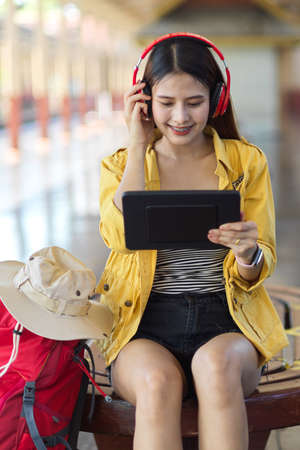 Portrait of female traveller with headphone and digital tablet while sitting in train stationの写真素材