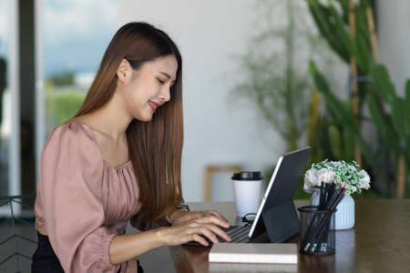 Side view of young female using digital tablet and stationery in relaxing corner at officeの写真素材