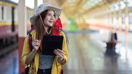 Half-length portrait of young female backpacker smiling while looking for her destination in train stationの写真素材