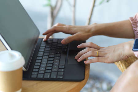 Side view of female hands typing on tablet keyboard on coffee table in relaxing corner at officeの写真素材