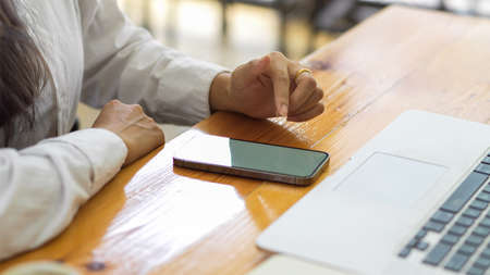 Side view of view of female hand using smartphone with mock-up screen on wooden table