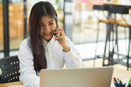 Young female talking on the phone while working with laptop in office roomの写真素材