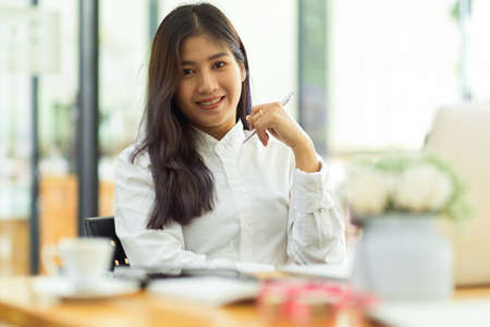 Portrait of young female worker smiling to camera while sitting in workplaceの写真素材