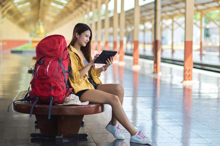 Side view of young female traveller using digital tablet while waiting for the train at platformの写真素材