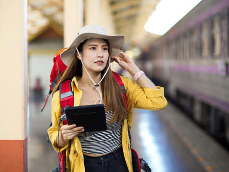 Portrait of female backpacker with backpack and digital tablet looking for her destination in train stationの写真素材