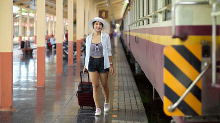 Full-length portrait of young beautiful female traveller with suitcase walking in train stationの写真素材