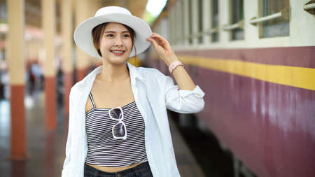 Half-length portrait of young beautiful female traveller smiling while standing at train stationの写真素材