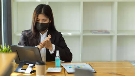 Businesswoman with medical mask hands sanitising with alcohol gel before start doing her workの写真素材