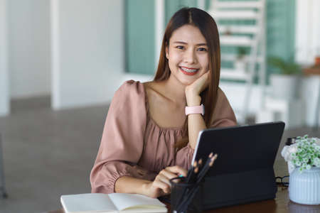 Portrait of young female worker smiling to camera while working with digital tablet in cafeの写真素材