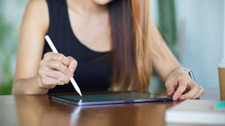 Cropped shot of young female hand with stylus pen touching on digital tablet screen on wooden tableの写真素材