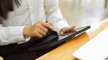 Cropped shot of female worker using digital tablet while sitting at workplace