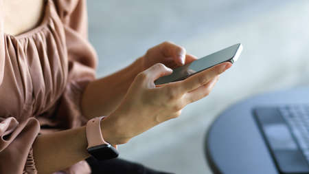Side view of female worker hands texting message on smartphone in workplaceの写真素材