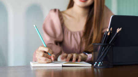 Cropped shot of female hand writing on notebook, planning her schedule on wooden tableの写真素材