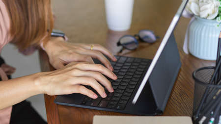 Close up view of female worker hands typing on tablet keyboard on wooden table with stationeryの写真素材