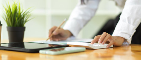 Close up view of businesswoman hands working with calculator and paperwork on office deskの写真素材