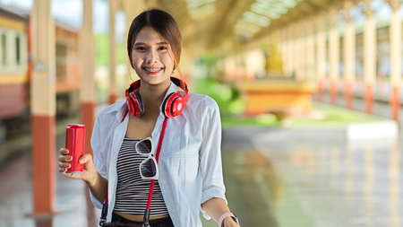 Portrait of female traveller with travel items holding beverage can and smiling to cameraの写真素材