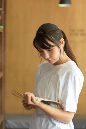Portrait of young female student reading a book while searching book for her project in libraryの写真素材