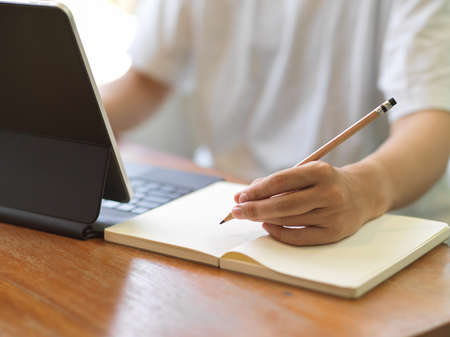 Close up view of female hand with pencil working on notebook and digital tablet on wooden tableの写真素材