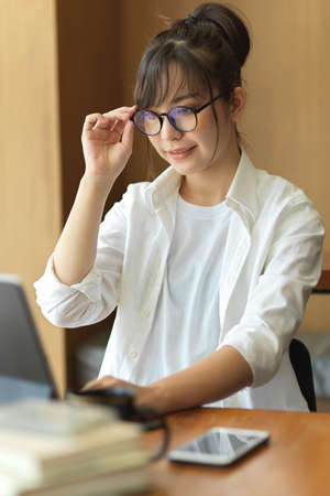 Young pretty female student with eyeglasses preparing for upcoming exam with digital tablet in cafeの写真素材