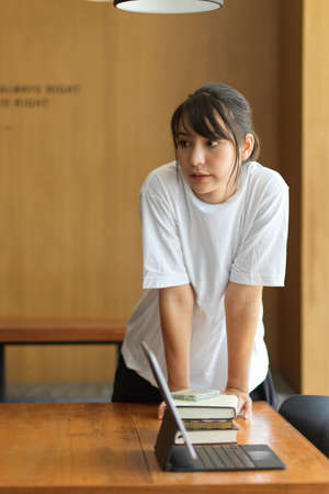 Quarter-length portrait of young female student standing at workspace in libraryの写真素材