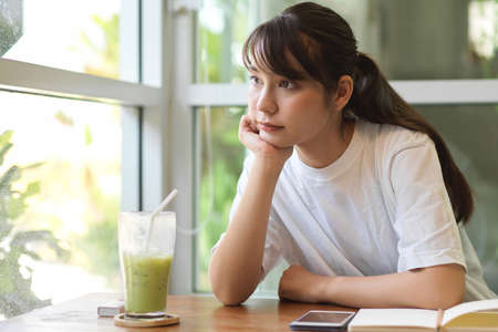 Portrait of young female teenager looking out of the window and thinking about her assignmentの写真素材