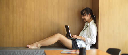Young pretty female using digital tablet on her lap while relaxed sitting in reading cornerの写真素材